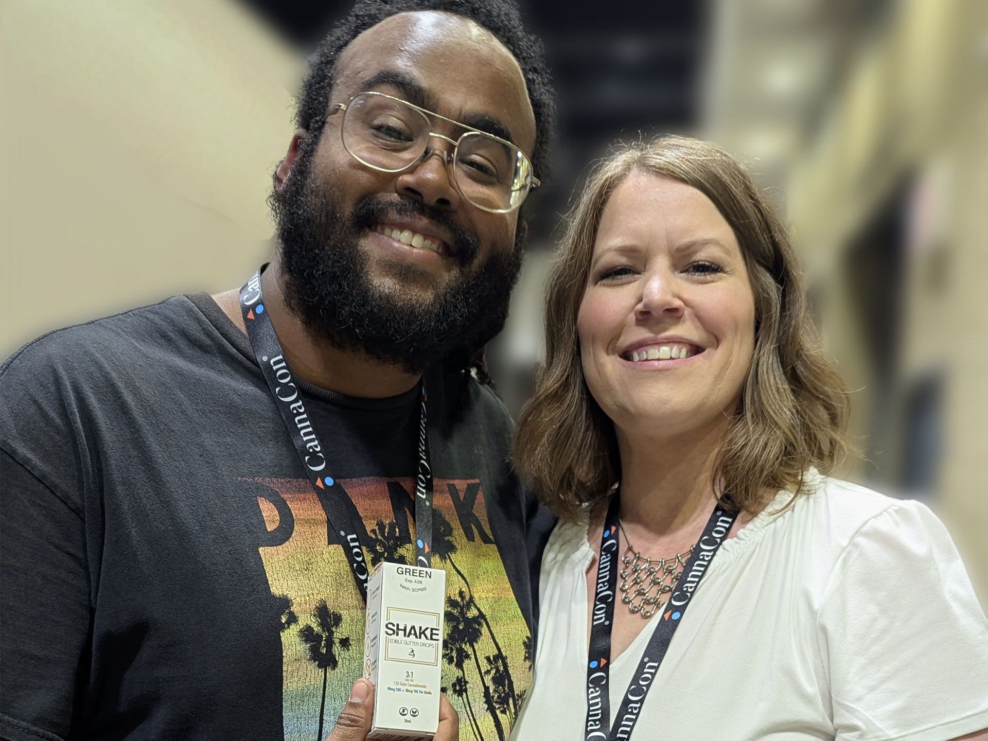 Two people standing close together, smiling, with a box of SHAKE infused edible glitter drops