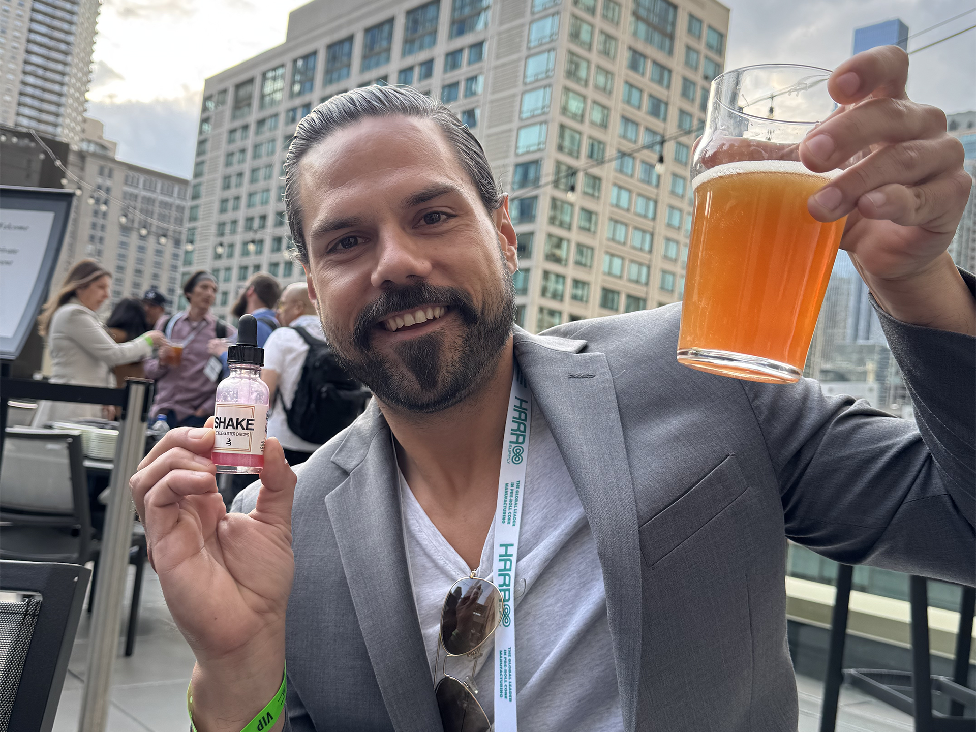 Man holding a glass of beer and a bottle of Pink SHAKE with a cityscape background.