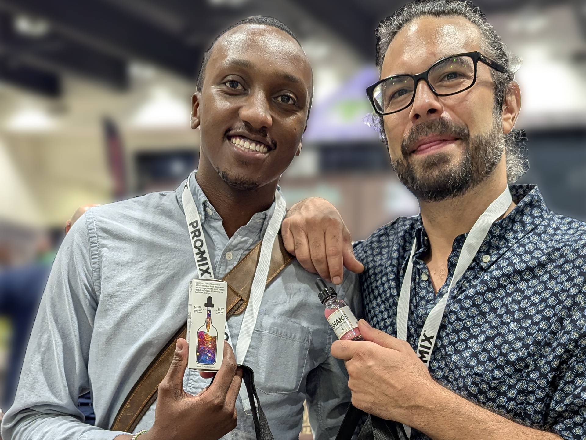 Two men holding SHAKE infused edible glitter and a box at a cannabis event.