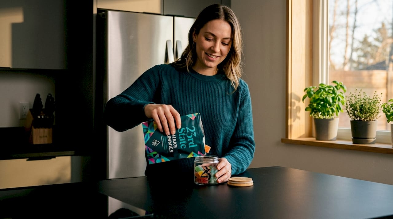 Person storing gummies in glass jar on kitchen counter