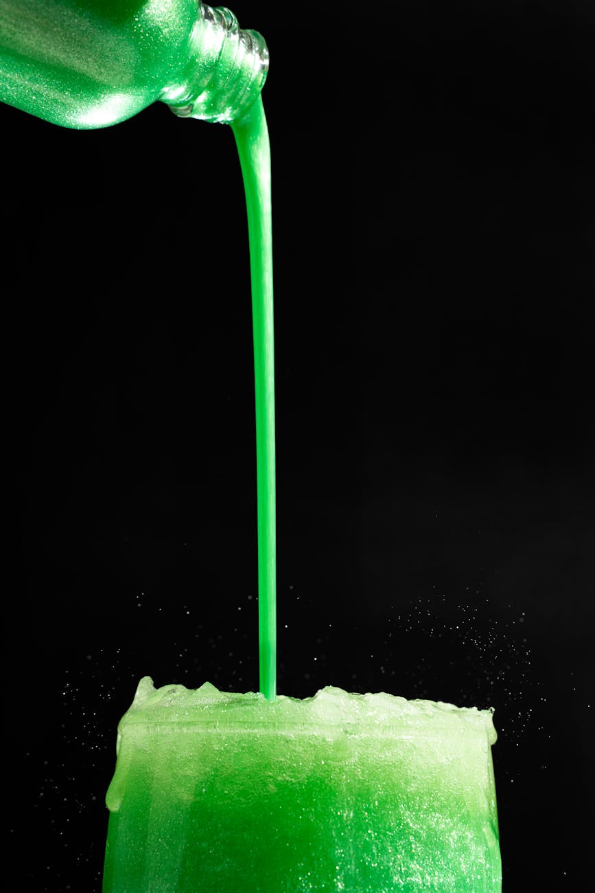 Edible glitter being poured into a bright green drink on a black background