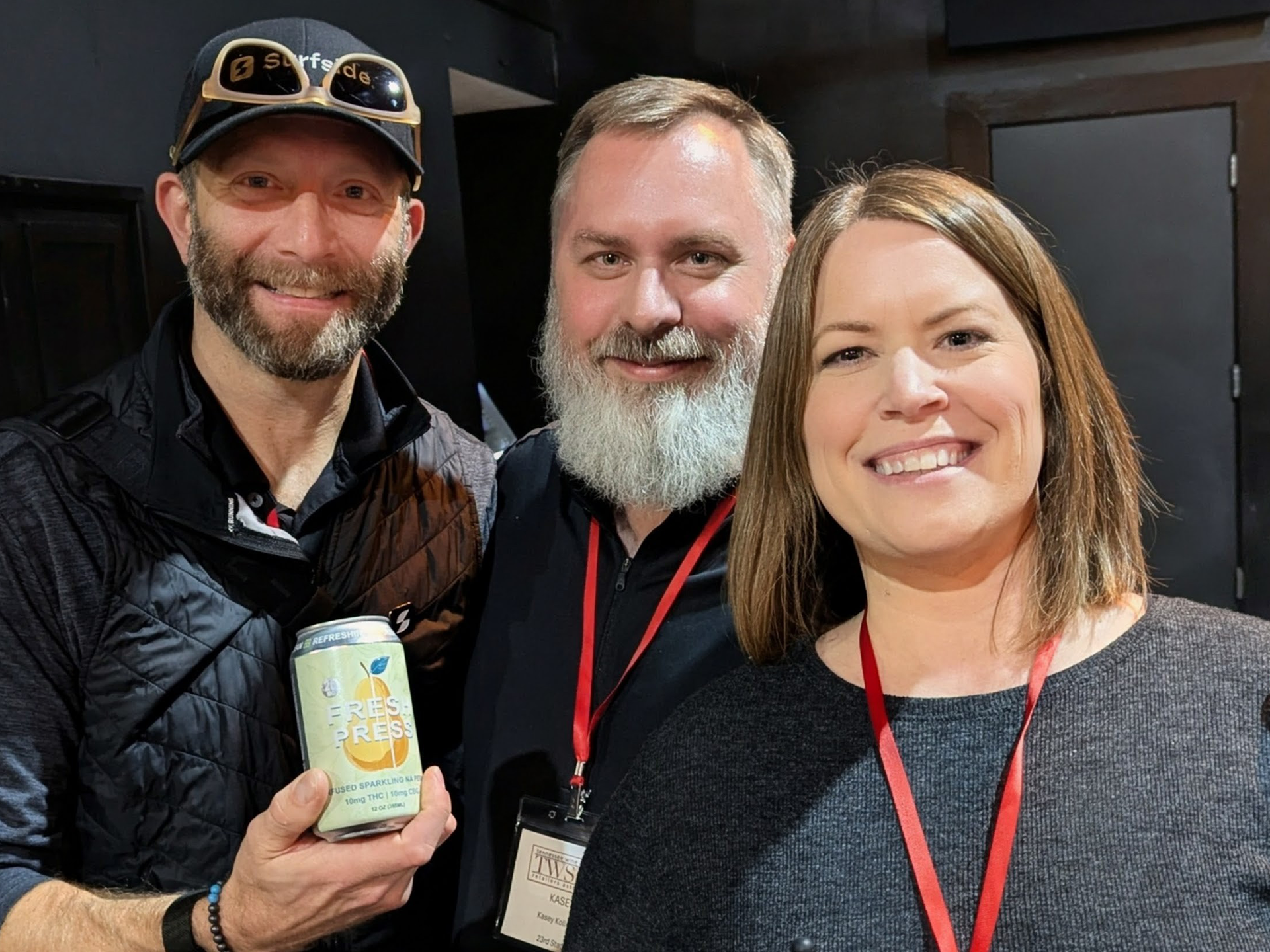 23rd State team photo of three people posing together, one holding a can of Fresh Press, indoors. 