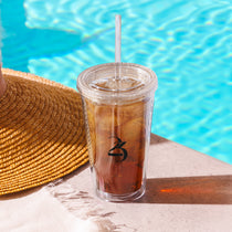Clear tumbler with THC infused iced tea and straw next to a straw hat by a pool